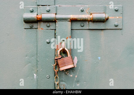 Closed rusted padlock blocking deadbolt on green steel door. Stock Photo