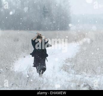 running samurai wearing a kimono in a winter field dressed in black, frost Stock Photo