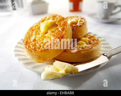 Traditional hot buttered toasted crumpets on a white plate on a table setting, with melted butter ready to eat Stock Photo