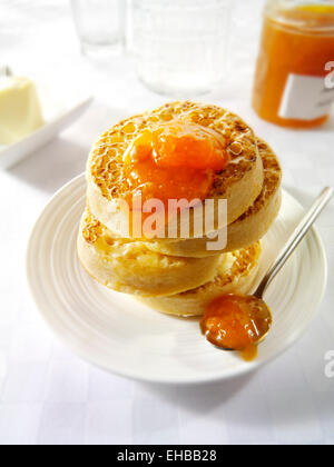 Close up of buttered toasted crumpets with apricot jam ready to eat in a white table setting Stock Photo