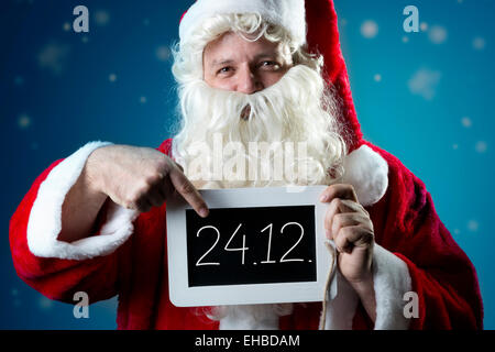 Santa Claus pointing a finger on a blank slate with text 24.12. Stock Photo