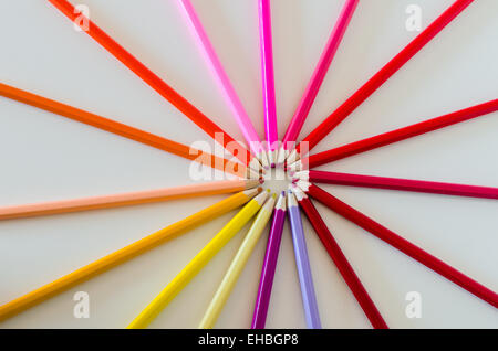 Brightly colored pencil crayons from the red side of the colour spectrum are arranged into a circle or wheel making a burst or Stock Photo