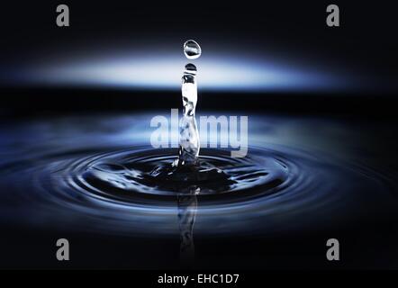 Water drop creating waves and ripples in on a dark blue background. Stock Photo