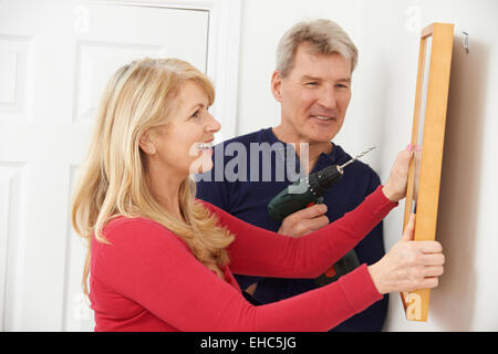 Mature Couple Drilling Wall To Hang Picture Frame Stock Photo