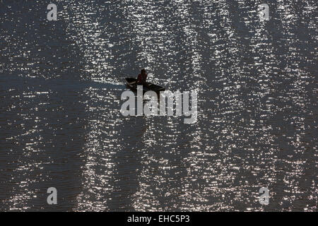 Local canoe being paddled on a sun spangled River Amazon paddler silhouetted against the water with small waves Amazonia Brazil Stock Photo