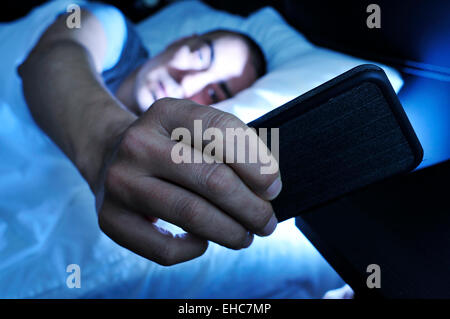 closeup of a young man in bed looking at the smartphone at night Stock Photo