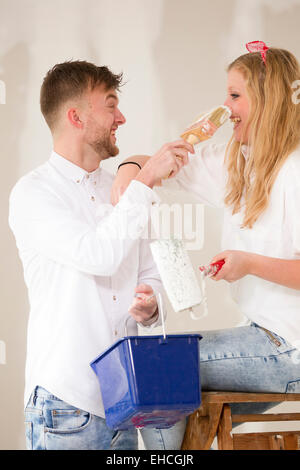 Pretty happy young couple working in their new home, platering a wall. Stock Photo