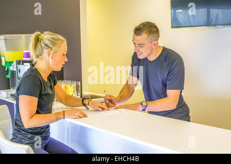 Young woman filling in a registration form with help from man at a desk in health club Stock Photo