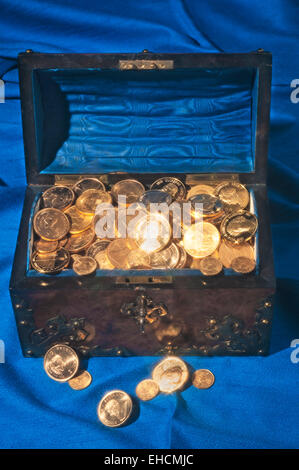 Chest filled with gold coins, on blue fabric Stock Photo