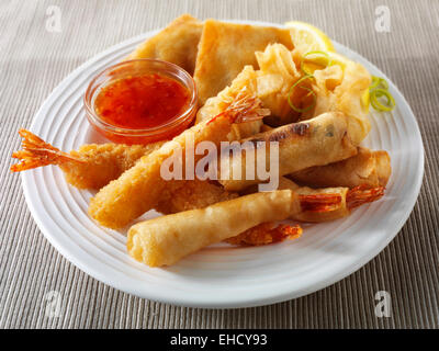 Cooked mixed Chinese starters - Dim sum, breaded prawns, spring rolls with chilli sauce served on a white plate Stock Photo