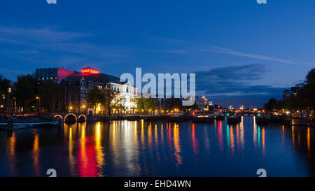 A view of the river Amstel in Amsterdam after the sun has set and the sky is a deep blue. The city's skyline is illuminated. Stock Photo