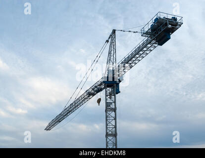White and blue construction crane facing left against overcast gray sky. Stock Photo