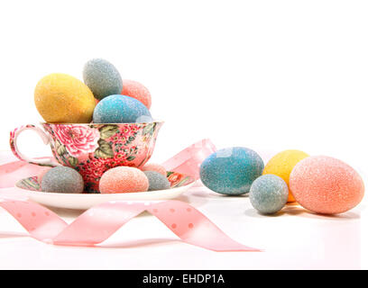 Brightly colored eggs in tea cup on white Brightly colored eggs in tea cup on white