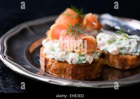 Canapes with smoked salmon and cream cheese spread on vintage metal plate, selective focus Stock Photo