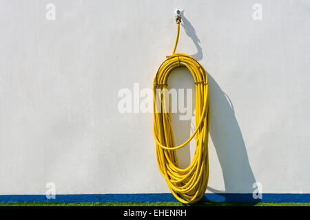 Yellow hose hanging from a white wall Stock Photo