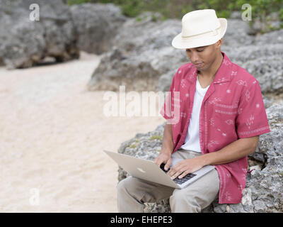 Man using Apple Macbook Air portable laptop computer to work on the beach while on holiday Stock Photo
