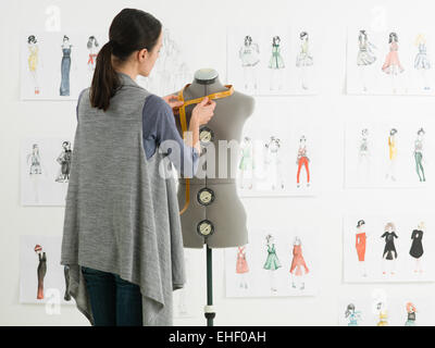 young caucasian female fashion designer taking measurements on mannequin in her studio Stock Photo