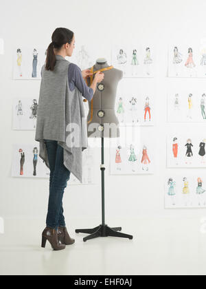 young caucasian female fashion designer taking measurements on mannequin in her studio Stock Photo