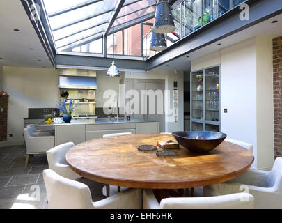 Round wooden table with chairs in glass roofed kitchen and dining area in The Organ Factory home, UK Stock Photo