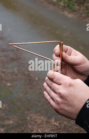 A water engineer uses copper divining rods to trace the course of an underground pipe (UK), a practice known as dowsing Stock Photo