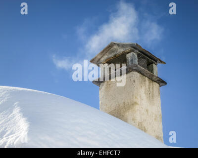 Smoke spreading from old mountain chimney on snowy roof. Vintage, old house on the mountain in winter. Warm and cold. Stock Photo