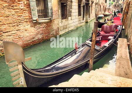 Small canal with parked gondola in Venice, Italy, waiting for tourists. Old medieval buildings and docked boats in a row. Stock Photo