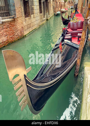 Small canal with parked gondola in Venice, Italy, waiting for tourists. Old medieval buildings and docked boats in a row. Stock Photo