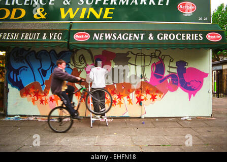 A graffiti artist and a boy doing a wheelie on his bike Camden Stock Photo