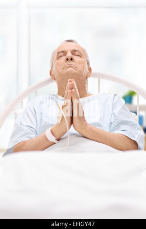 Senior patient lying in hospital bed and praying to god Stock Photo
