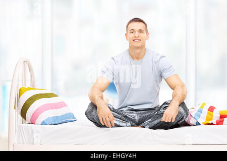 Young man in pajamas sitting on a bed at home Stock Photo