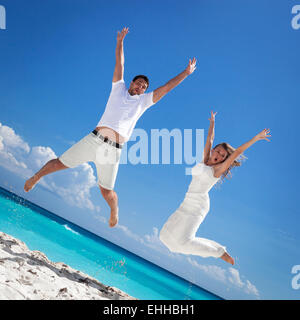 Happy newlyweds jumping up on beach with blue sky background Stock Photo