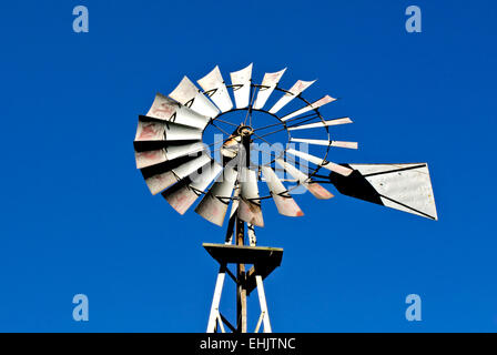 Antique western rusty metal windmill against clear blue sky. Stock Photo