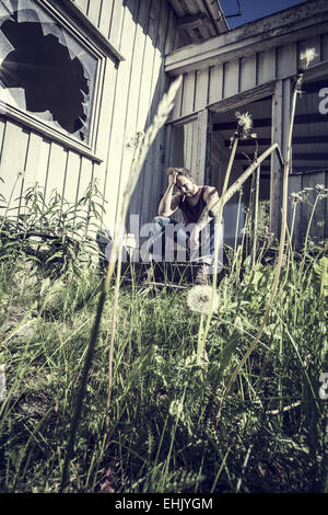 A young man sitting outside a abandoned house and smoke cigarettes. Stock Photo