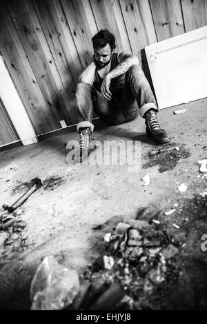 Punk rocker or redneck sits on the floor and think in messy house. Stock Photo