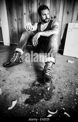 Punk rocker or redneck sits on the floor and smoke in a messy house. Stock Photo