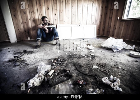 Man or redneck sits on the floor and smoke in a messy house. Stock Photo