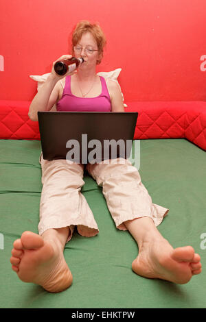 woman with laptop sitting on her bed Stock Photo