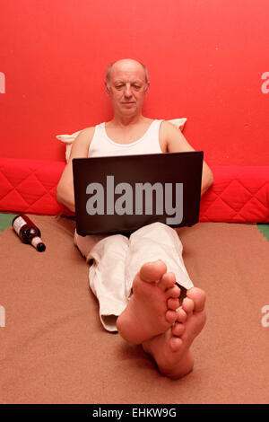 man sitting in his bed with his laptop on his lap Stock Photo