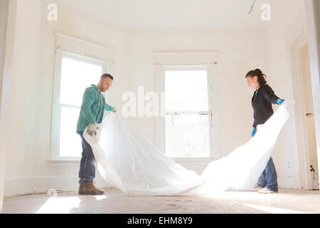 Mixed race couple spreading tarp in new home Stock Photo