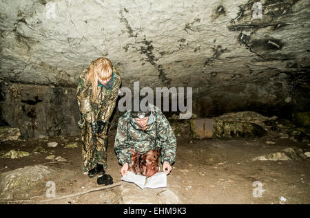 Caucasian hunters in camouflage crouching in rock cave Stock Photo