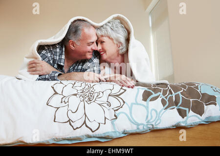 Older couple rubbing noses under blanket on bed Stock Photo