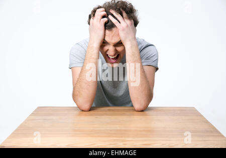 Upset young man sitting at the wooden table Stock Photo