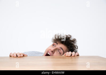 Scary young man peeking from behind the desk Stock Photo