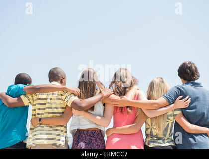 Rear view of teenagers hugging under blue sky Stock Photo