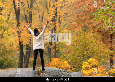 Asian woman cheering with arms outstretched on rock in park Stock Photo