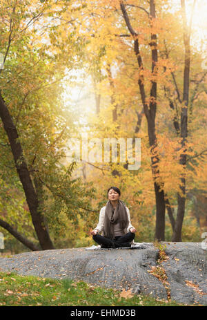 Asian woman meditating on rock in park