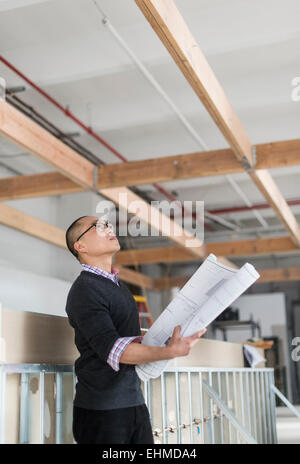Korean architect holding blueprints and examining ceiling Stock Photo