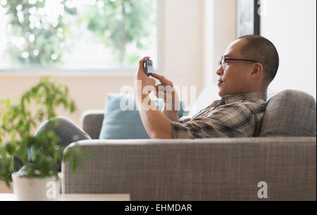 Korean man using cell phone on sofa Stock Photo