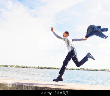 Black businessman running on waterfront wall outdoors Stock Photo