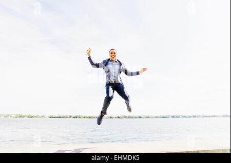 Black businessman jumping for joy at waterfront Stock Photo
